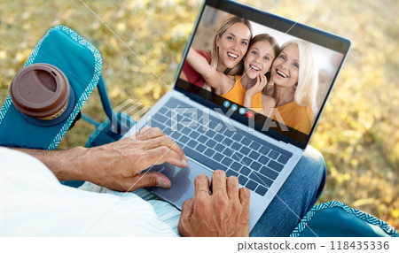 A senior man sits on a blue lawn chair outdoors and uses a laptop to have a video call with his family. He is smiling and appears happy to be connected to his loved ones A senior man sits on a blue lawn chair outdoors and uses a laptop to have a video call with his family. He is smiling and appears happy to be connected to his loved ones 118435336