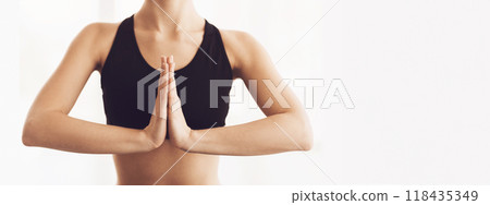 A woman is captured in a moment of tranquility, her hands pressed together in a Namaste gesture, a common yoga pose. The focus on her hands and the soft, cropped, panorama with copy space 118435349