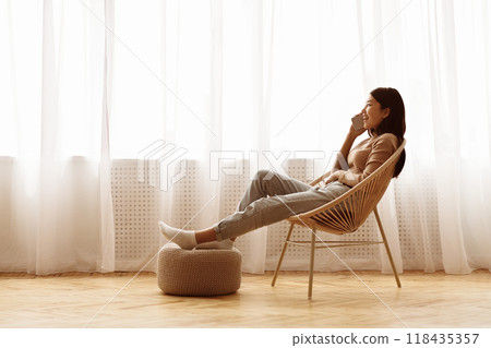 Relaxed Girl Talking on Phone near Window, Sitting on Chair and Resting, Free Space Relaxed Girl Talking on Phone near Window, Sitting on Chair and Resting, Free Space 118435357