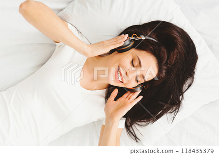 Personal relax. Young millennial woman listening to music, lying in bed in wireless headphones, top view 118435379