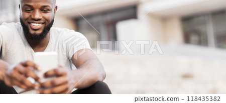 A man with a beard smiles while using his smartphone outdoors. 118435382
