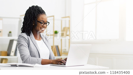 Positive African American businesswoman working at her desk with a laptop, writing notes in a modern office environment, copy space Positive African American businesswoman working at her desk with a laptop, writing notes in a modern office environment, copy space 118435400
