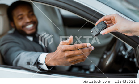 A man sits in the drivers seat of a new car, extending his hand to receive the keys from someone outside the vehicle. He is smiling and appears to be happy and excited about his new car. A man sits in the drivers seat of a new car, extending his hand to receive the keys from someone outside the vehicle. He is smiling and appears to be happy and excited about his new car. 118435521