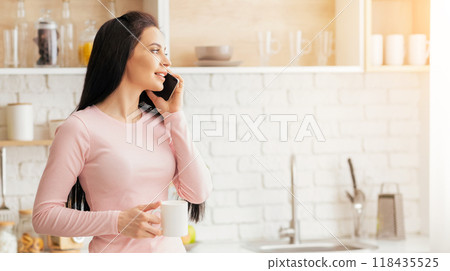 A woman in a pink dress is engaged in a phone conversation, holding a cell phone to her ear. She appears to be focused on the call, standing in a casual pose. 118435525