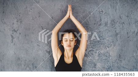 A woman dressed in a black top is practicing yoga poses in a room. She is focused and performing various stretches and poses on a yoga mat. A woman dressed in a black top is practicing yoga poses in a room. She is focused and performing various stretches and poses on a yoga mat. 118435563