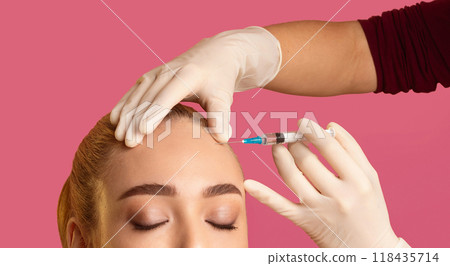 A close-up image of a woman receiving an injection in her forehead from a medical professional wearing white gloves. The woman has her eyes closed and is relaxed, with her hair pulled back A close-up image of a woman receiving an injection in her forehead from a medical professional wearing white gloves. The woman has her eyes closed and is relaxed, with her hair pulled back 118435714