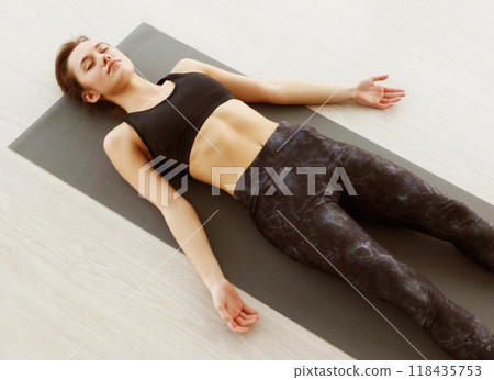 A woman is laying on a yoga mat, engaging in relaxation and stretching exercises. She is in a comfortable and meditative position, focusing on her breath and body alignment. A woman is laying on a yoga mat, engaging in relaxation and stretching exercises. She is in a comfortable and meditative position, focusing on her breath and body alignment. 118435753