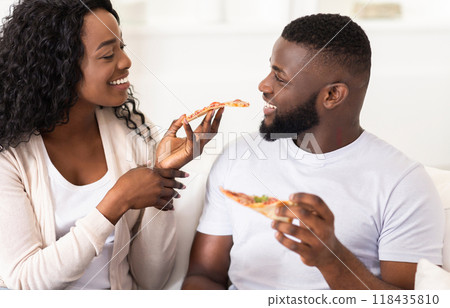 A couple shares a slice of pizza while smiling at each other. 118435810