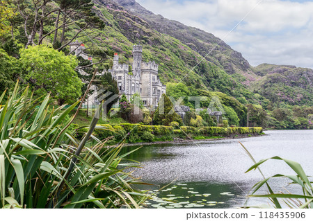 A side view of Kylemore Abbey in Connemara, Ireland, partially obscured by lush foliage 118435906