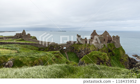Panoramic view of Dunluce Castle on cliff, steep grassy slopes and rugged terrain around 118435952