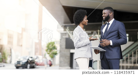 Attractive african american coworkers having pleasant chat while standing against office center, copy space 118435971