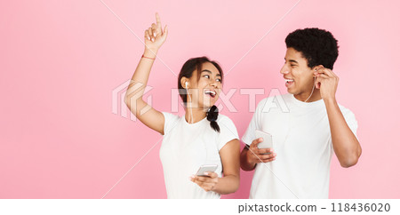 Happy students dancing and listening music by earphones over pink studio background Happy students dancing and listening music by earphones over pink studio background 118436020