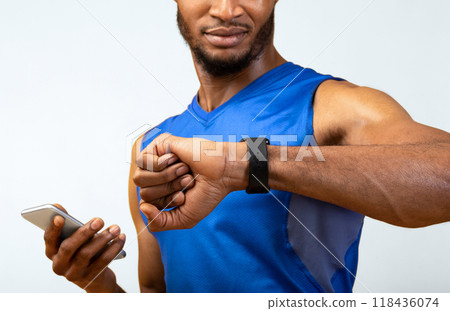 Fitness Tracker. Portrait of afro muscular man holding mobile phone and looking at smartwatch, yellow wall, copyspace Fitness Tracker. Portrait of afro muscular man holding mobile phone and looking at smartwatch, yellow wall, copyspace 118436074