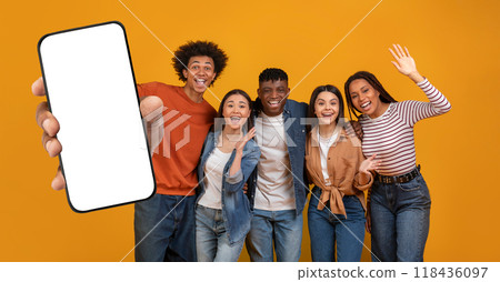 Five multiethnic friends stand together, smiling and posing enthusiastically, with one holding up a blank smartphone. The cheerful atmosphere is highlighted by a vibrant yellow backdrop. Five multiethnic friends stand together, smiling and posing enthusiastically, with one holding up a blank smartphone. The cheerful atmosphere is highlighted by a vibrant yellow backdrop. 118436097