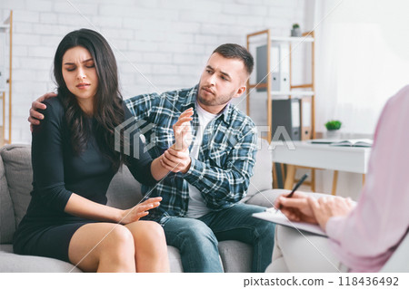 This image depicts a couple sitting on a couch in a therapists office, presumably receiving marriage counseling. The woman in the image appears to be visibly upset 118436492