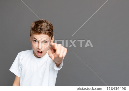 A young boy with an assertive expression points directly at the camera, conveying directness or accusation, standing isolated against a grey background 118436498