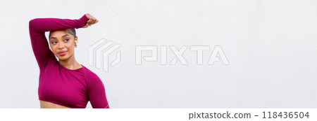 Athletic young black woman exercising on white background. Confident lady training over empty wall, wearing pink sportswear, holding bottle of water, looking at copy space. Hydration during workout 118436504