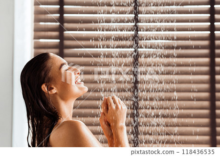 Young woman taking refreshing shower, standing under water drops, side view Young woman taking refreshing shower, standing under water drops, side view 118436535