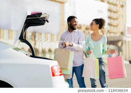 African American happy couple, dressed casually in jeans and shirts, are walking towards their car with a large number of shopping bags in their hands. 118436634