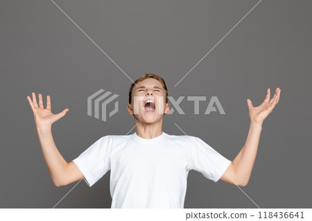 A teen boy stands isolated on a gray background with arms open wide in a stance that could symbolize freedom or surprise 118436641