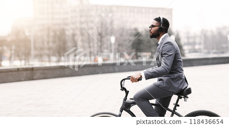 An African American businessman is cycling to the office through a modern city. The scene is dynamic and bustling, showcasing a balance between professional life and eco-friendly commuting. 118436654