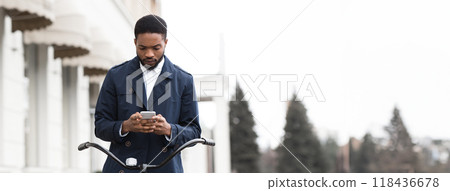 An African American businessman is commuting to the office on his bicycle while using his phone. The scene is energetic and dynamic, capturing the balance of modern work and active lifestyle. 118436678