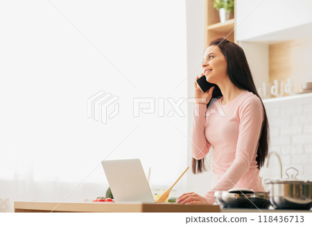 A woman is multitasking by talking on a phone and using a laptop simultaneously. She appears focused and engaged in both activities. 118436713