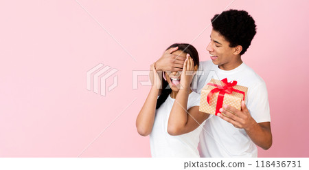 Loving guy closing lady's eyes preparing gift over pink studio background, crop 118436731