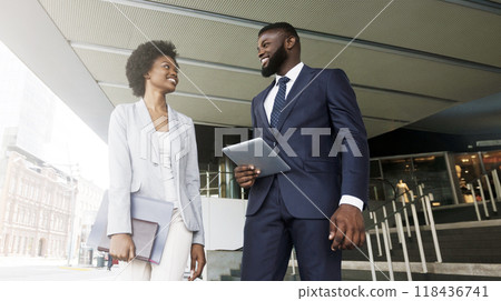 Two smiling african american colleagues discussing new project while going out of office building, copy space 118436741
