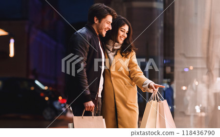 A couple standing in front of a store, holding shopping bags filled with purchases. 118436790