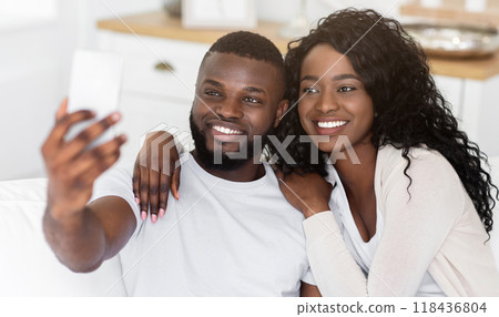 A happy couple takes a selfie together while sitting on a couch in their living room. A happy couple takes a selfie together while sitting on a couch in their living room. 118436804