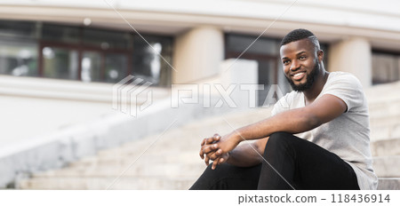 A young man sits on a set of city steps, smiling and looking off to the side. A young man sits on a set of city steps, smiling and looking off to the side. 118436914