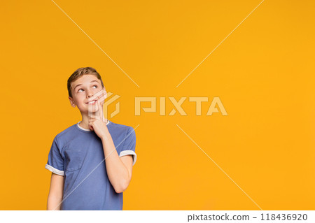 Tricky boy thinking about some prank, looking up at free space on orange background 118436920