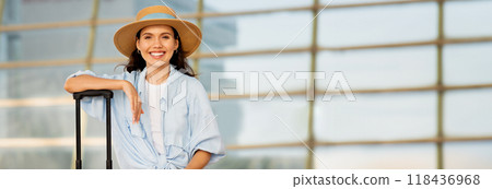 Positive young european lady tourist in hat with suitcase, uses enjoy journey, wait transport on train station. Trip, active lifestyle, vacation in summer, copy space Positive young european lady tourist in hat with suitcase, uses enjoy journey, wait transport on train station. Trip, active lifestyle, vacation in summer, copy space 118436968