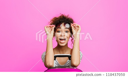 Surprised tourist leaning on suitcase and looking at camera over pink background Surprised tourist leaning on suitcase and looking at camera over pink background 118437050