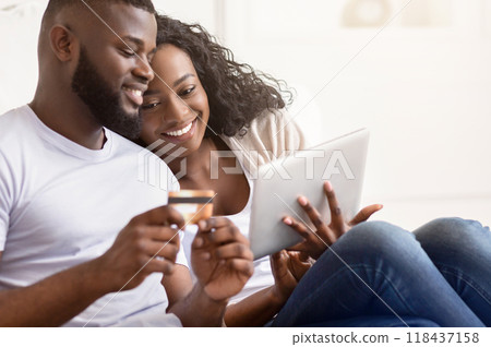 A couple smiles and looks at a tablet while shopping online. The woman holds a credit card in her hand. A couple smiles and looks at a tablet while shopping online. The woman holds a credit card in her hand. 118437158