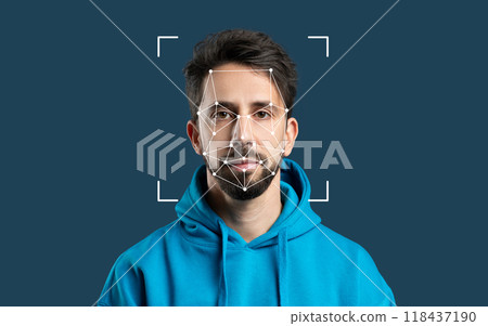 A man wears a blue hoodie as facial recognition technology analyzes his features against a solid dark backdrop. 118437190