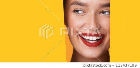 A woman face is partially visible through a round hole in a bright yellow background. She appears to be looking directly at copy space, with a neutral expression, panorama 118437199