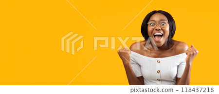 Happy Black Woman Screaming Shaking Fists Celebrating Success Standing Over Orange Studio Background. Panorama, Empty Space Happy Black Woman Screaming Shaking Fists Celebrating Success Standing Over Orange Studio Background. Panorama, Empty Space 118437218