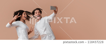 Selfie Fun. Millennial Interracial Couple Jumping And Taking Self-Portrait, Posing Together Over Yellow Background, Afro Girl Showing Peace Gestures 118437228