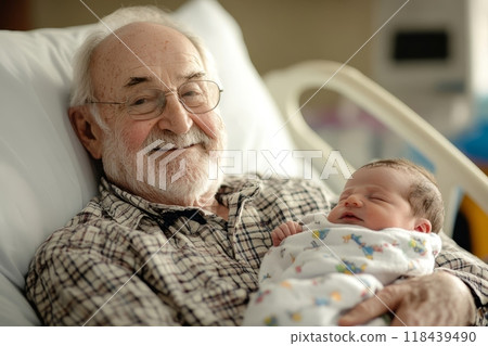 A smiling elderly man with white hair and beard holds a sleeping newborn baby in a hospital bed, capturing a heartwarming moment between generations 118439490