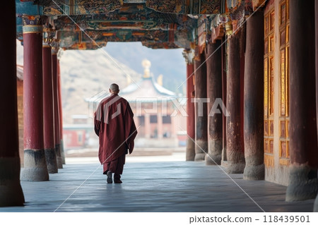 A Buddhist monk in red robes walking through an ornate temple corridor with colorful decorations and pillars, mountains visible in the background 118439501