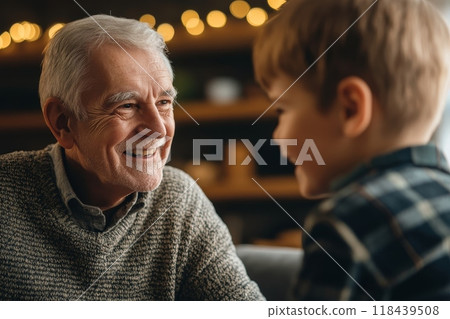 Smiling elderly man in a sweater looking lovingly at his young grandson, with warm lighting and bokeh background suggesting a cozy home setting 118439508