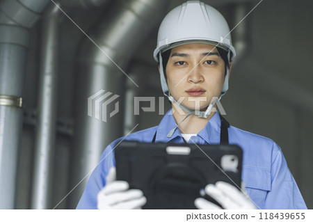 Building maintenance image: A man carrying a tablet while carrying out inspection work, looking at the camera Building maintenance image: A man carrying a tablet while carrying out inspection work, looking at the camera 118439655