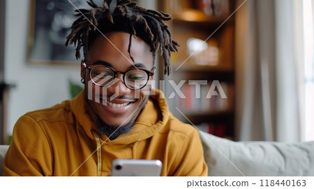 A young man in a hoodie engages in a friendly video call, smiling while seated on a couch in a bright, inviting living room 118440163