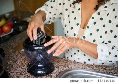 Woman using electric juicer in kitchen, preparing fresh citrus juice on a granite countertop, wearing polka dot shirt, with bowl of apples in the background. Woman using electric juicer in kitchen, preparing fresh citrus juice on a granite countertop, wearing polka dot shirt, with bowl of apples in the background. 118440450