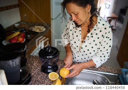 Woman preparing fresh lemon juice in a cozy kitchen with fruits on the counter and a juicer, showcasing a healthy and natural lifestyle. Woman preparing fresh lemon juice in a cozy kitchen with fruits on the counter and a juicer, showcasing a healthy and natural lifestyle. 118440456