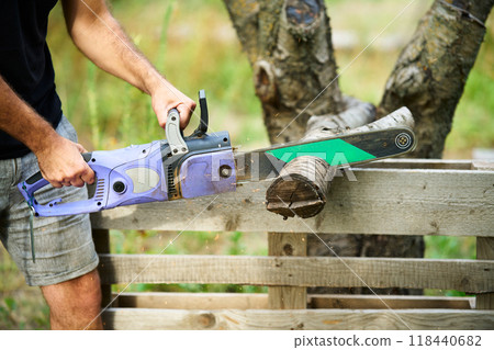 Close-up of man cutting trees using electrical chainsaw in motion 118440682