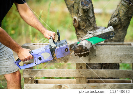 Close-up of man cutting trees using electrical chainsaw in motion 118440683