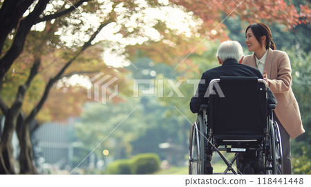 Elderly person in wheelchair walking with female helper 118441448
